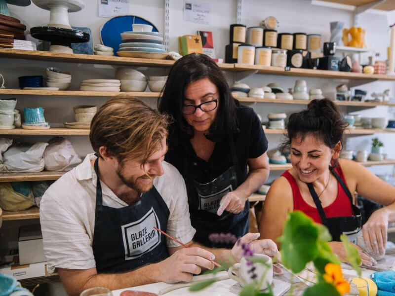 A man and a woman smiling as they learn how to cut clay to make a pot